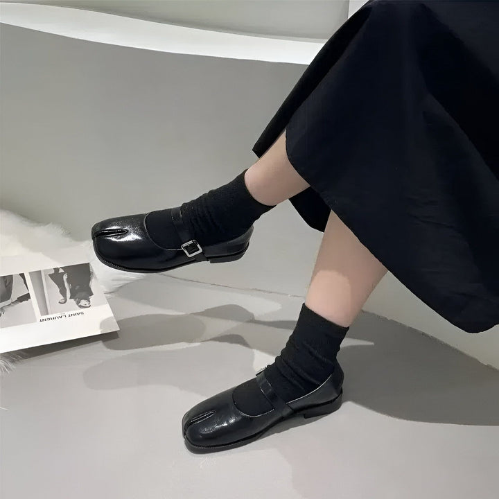 Gros plan sur des chaussures Mary Jane en cuir noir avec un bout fendu "tabi", portées avec des chaussettes noires et une jupe noire. Style avant-gardiste., 45286636585141,45286636617909,45286636650677,45286636683445,45286636716213,45286636748981