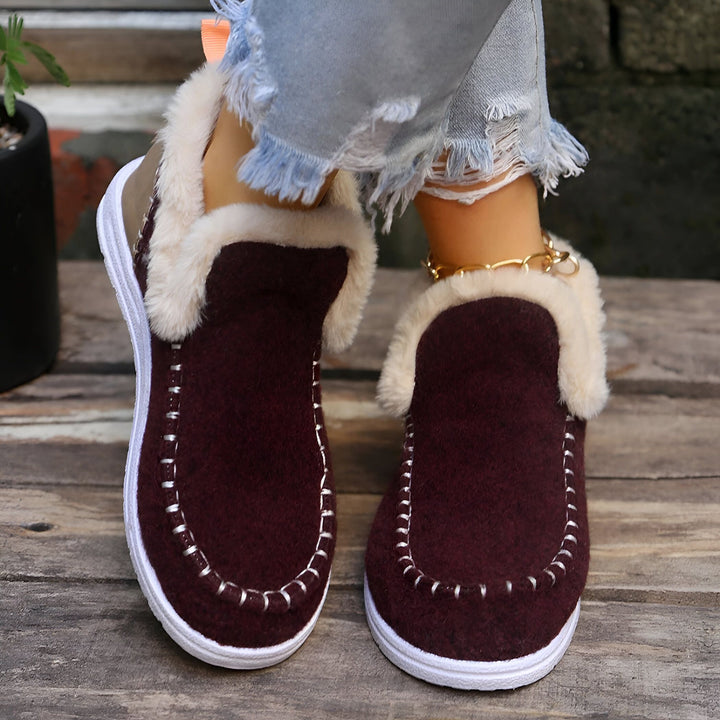 Gros plan sur des chaussons d'intérieur bordeaux doublés de fourrure portés avec un jean effiloché et une chaîne de cheville dorée. Chaussons confortables et élégants., 45286658375861