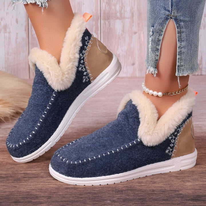 Vue rapprochée de pantoufles d'intérieur bleues à doublure en fourrure portées avec un jean décontracté et une cheville ornée d'un bracelet fantaisie, sur un parquet en bois. Chaussons confortables et tendance pour se détendre à la maison., 45286658375861