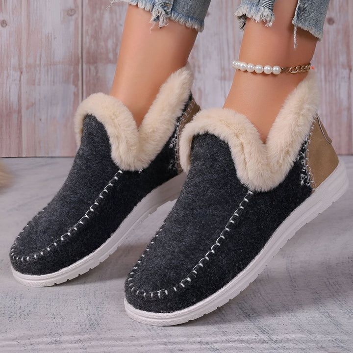 Vue rapprochée de chaussons d'intérieur gris anthracite avec doublure en fausse fourrure beige, portés par une personne avec un jean déchiré et une chaîne de cheville perlée. Chaussures confortables pour femmes, style décontracté., 45286658375861