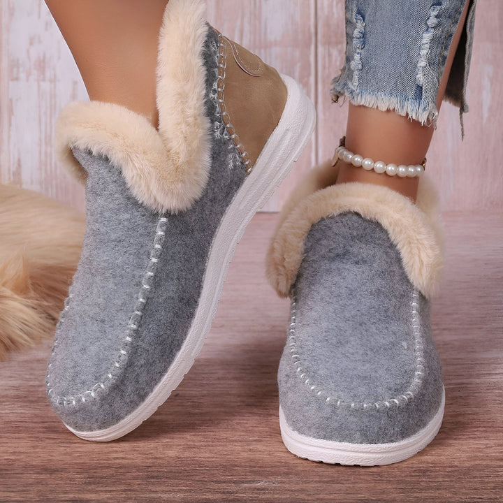 Gros plan de chaussons gris en feutre avec doublure en fausse fourrure crème. Une femme porte des jeans déchirés et une chaîne de cheville perlée., 45286658375861