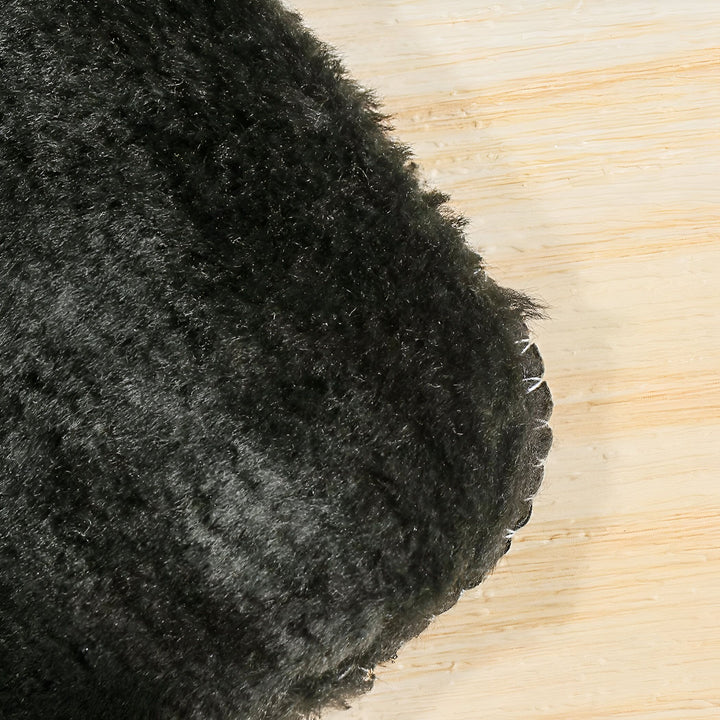 Gros plan d'un tapis en fausse fourrure noire sur un plancher en bois. Texture douce et moelleuse du tapis. Couture apparente sur le bord. Décoration intérieure., 45286864978101