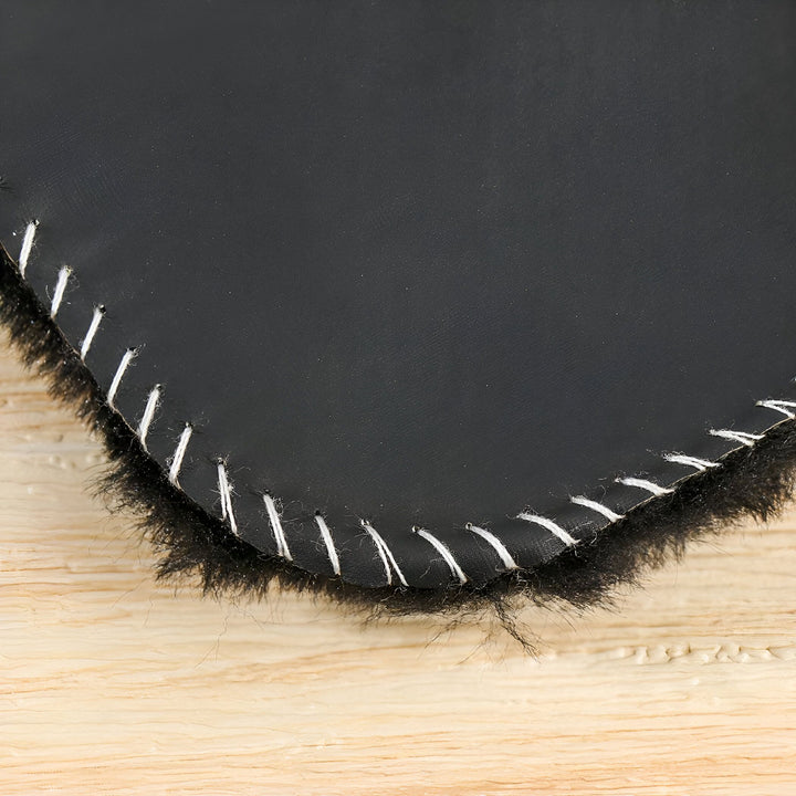 Gros plan d'une couverture noire en fausse fourrure, bordée de points blancs, posée sur une surface en bois clair. Texture douce et artisanale., 45286864978101