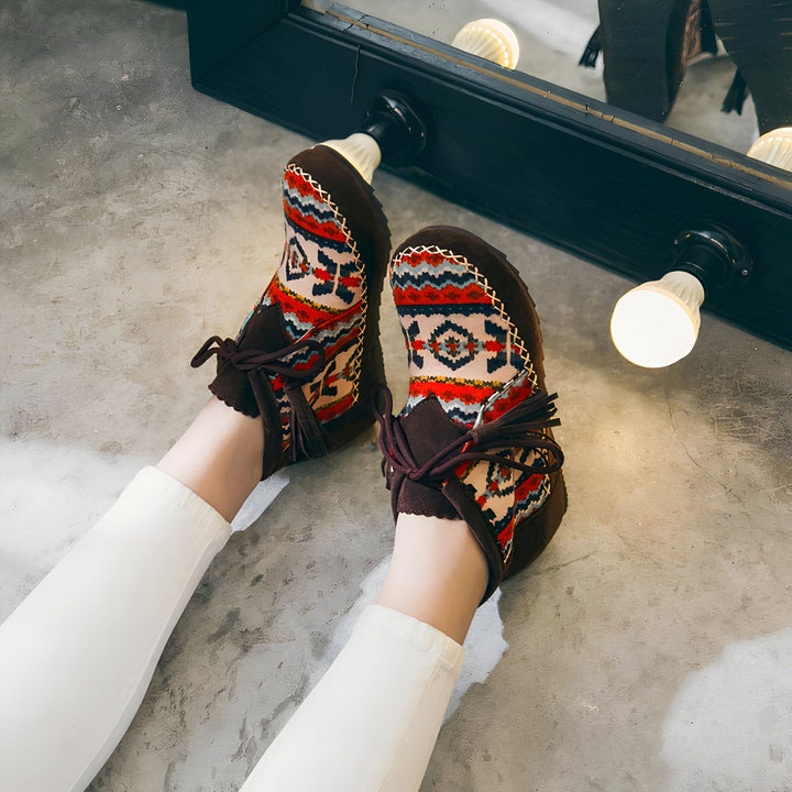 Vue de dessus d'une personne portant des bottines marron à motifs ethniques colorés. Les bottines ont des lacets marron et des pompons. La personne porte un pantalon blanc. En arrière-plan, on aperçoit un miroir avec des ampoules., 45286981632181,45286981664949,45286981697717,45286981730485,45286981763253,45286981796021,45286981828789,45286981861557,45286981894325,45286981927093,45286981959861,45286981992629,45286982025397,45286982058165,45286982090933,45286982123701,45286982156469,45286982189237,4528