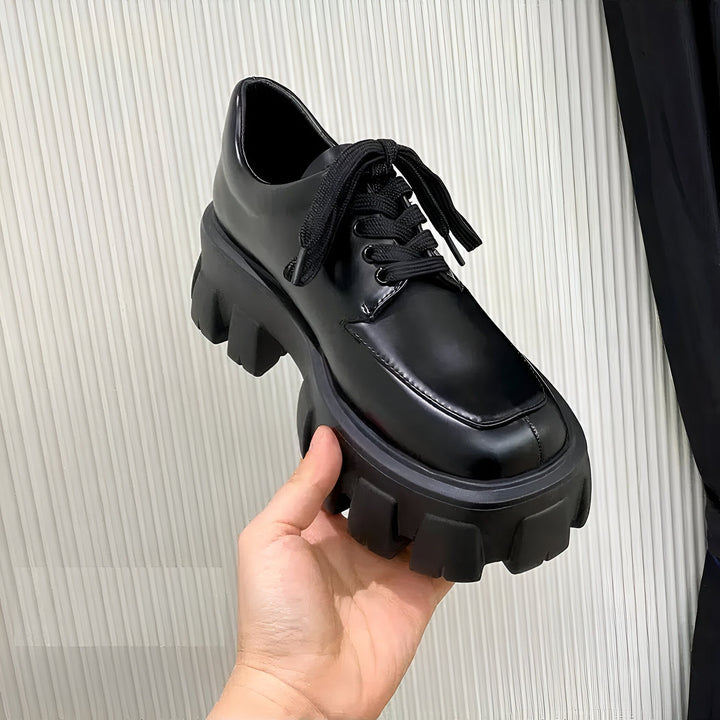 Chaussure derby noire vernie à lacets, semelle épaisse crantée. Une main la présente. Mode, tendance., 45286884180149,45286884212917,45286884245685,45286884278453,45286884311221,45286884343989,45286884376757,45286884409525,45286884442293,45286884475061