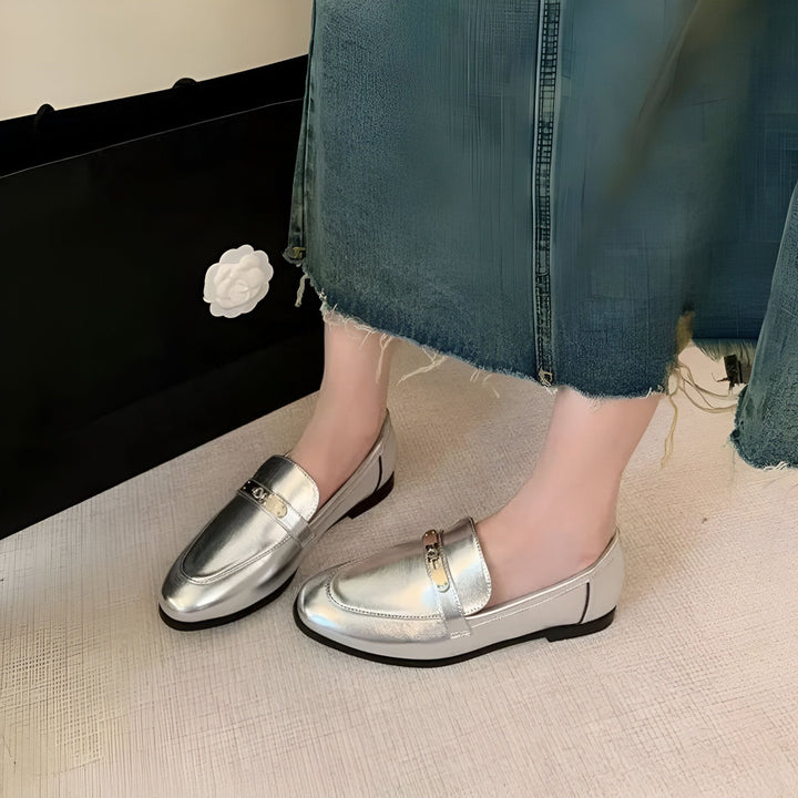 Gros plan de chaussures mocassins argentées portées avec une jupe en jean. Sac noir visible en arrière-plan. Style tendance et décontracté., 45286708412597,45286708445365,45286708478133,45286708510901,45286708543669