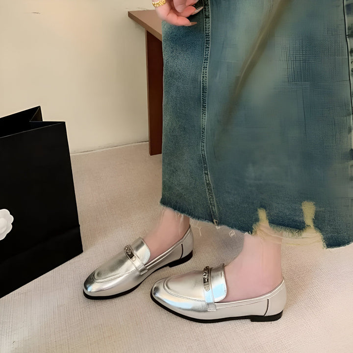 Gros plan de mocassins argentés avec un détail métallique doré, portés avec une longue jupe en jean bleu délavé. Sac de shopping noir à côté. Chaussures élégantes et confortables., 45286708412597,45286708445365,45286708478133,45286708510901,45286708543669