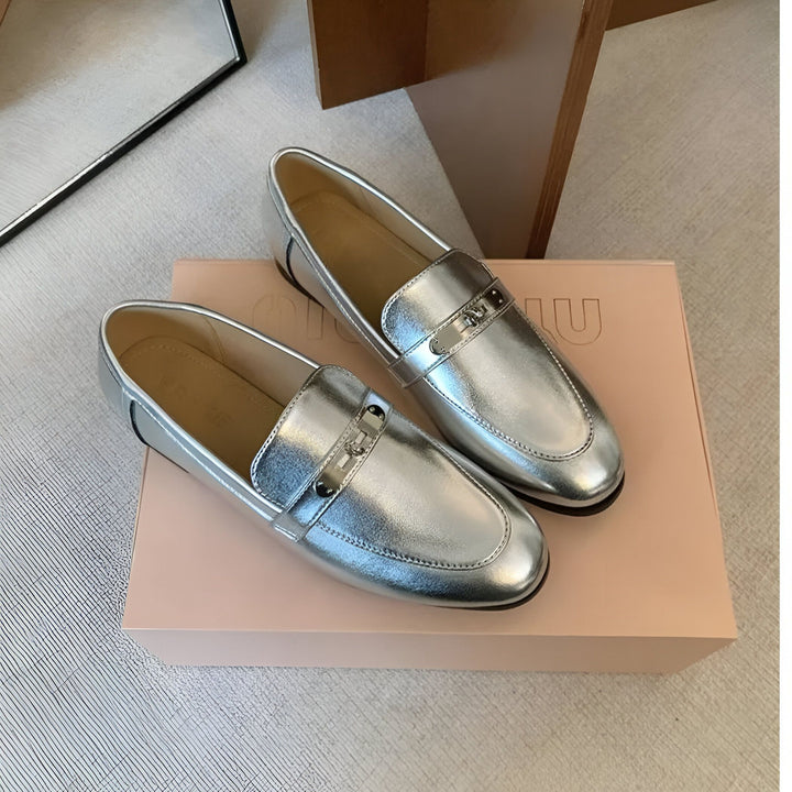 Deux mocassins argentés brillants sur une boîte rose pâle, avec une boucle métallique sur le dessus. Chaussures élégantes et modernes, parfaites pour une tenue décontractée ou habillée., 45286708412597,45286708445365,45286708478133,45286708510901,45286708543669