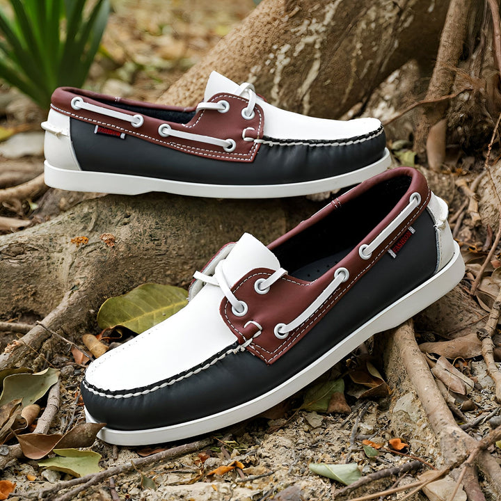 Deux chaussures bateau en cuir tricolore (blanc, marron, noir) posées sur des racines et feuilles. Lacets blancs. Style décontracté et nautique., 45287040745653,45287040778421,45287040811189,45287040843957,45287040876725,45287040909493,45287040942261,45287040975029