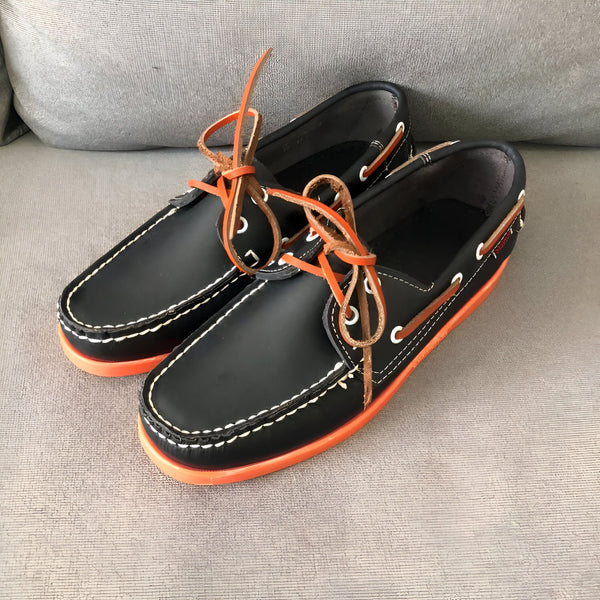 Paire de chaussures bateau en cuir noir avec lacets orange et semelles orange vif. Détails de couture blanche et logo de la marque visible., 45286756843701,45286756876469,45286756909237,45286756942005,45286756974773,45286757007541,45286757040309,45286757073077,45286757105845,45286757138613,45286757171381,45286757204149,45286757236917,45286757269685,45286757302453,45286757335221,45286757367989,45286757400757,45286757433525,45286757466293,45286757499061,45286757531829