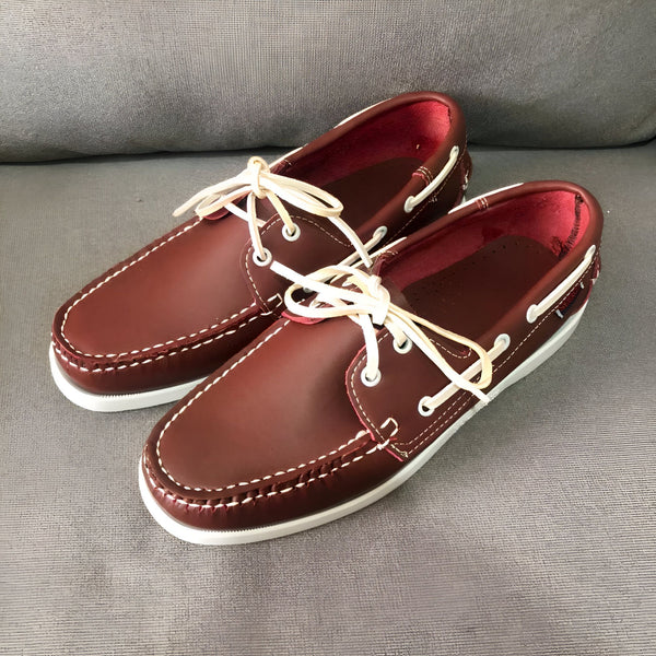 Une paire de chaussures bateau en cuir bordeaux avec des lacets blancs, posées sur un canapé gris. L'intérieur des chaussures est rouge. Les coutures sont blanches., 45286856458421,45286856491189,45286856523957,45286856556725,45286856589493,45286856622261,45286856655029,45286856687797,45286856720565,45286856753333,45286856786101,45286856818869,45286856851637,45286856884405,45286856917173,45286856949941,45286856982709,45286857015477,45286857048245,45286857081013,45286857113781,45286857146549,45286857179