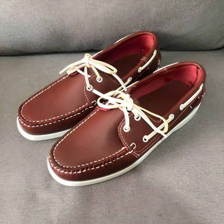 Une paire de chaussures bateau en cuir bordeaux avec des lacets blancs, posées sur un canapé gris. L'intérieur des chaussures est rouge. Les coutures sont blanches., 45286856458421,45286856491189,45286856523957,45286856556725,45286856589493,45286856622261,45286856655029,45286856687797,45286856720565,45286856753333,45286856786101,45286856818869,45286856851637,45286856884405,45286856917173,45286856949941,45286856982709,45286857015477,45286857048245,45286857081013,45286857113781,45286857146549,45286857179