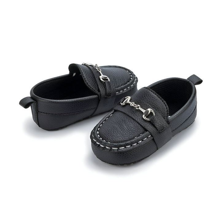 Chaussures bébé type mocassins noirs avec une boucle argentée sur le dessus. Petits souliers élégants pour enfant, vus de près. Chaussures en cuir noir, coutures blanches apparentes., 45286993789109,45286993821877,45286993854645,45286993887413,45286993920181,45286993952949,45286993985717,45286994018485,45286994051253