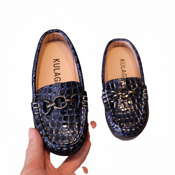Mocassins pour enfants bleu marine effet croco avec une boucle dorée, marque KULAG. Une main tient un mocassin, l'autre est à côté sur fond blanc. Chaussures élégantes pour garçons et filles., 45287067844789,45287067877557,45287067910325,45287067943093,45287067975861,45287068008629,45287068041397,45287068074165,45287068106933,45287068139701,45287068172469,45287068205237,45287068238005,45287068270773,45287068303541,45287068336309,45287068369077,45287068401845,45287068434613,45287068467381,4528706850