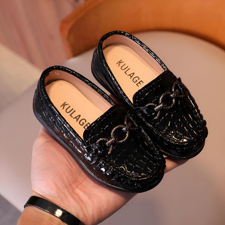 Mocassins noirs vernis pour enfants, avec détail de chaîne décorative, marque Kulage visible sur la semelle intérieure. Chaussures élégantes présentées dans une main., 45287067844789,45287067877557,45287067910325,45287067943093,45287067975861,45287068008629,45287068041397,45287068074165,45287068106933,45287068139701,45287068172469,45287068205237,45287068238005,45287068270773,45287068303541,45287068336309,45287068369077,45287068401845,45287068434613,45287068467381,45287068500149,45287068532917,4528