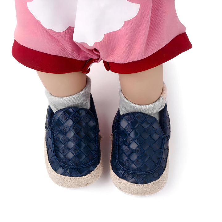 Gros plan des pieds d'un bébé portant des chaussures bleu marine à motifs et des chaussettes grises. Le bébé est vêtu d'une barboteuse rose et blanche., 45286948569269,45286948602037,45286948634805,45286948733109,45286948765877,45286948798645,45286948831413,45286948864181,45286948896949