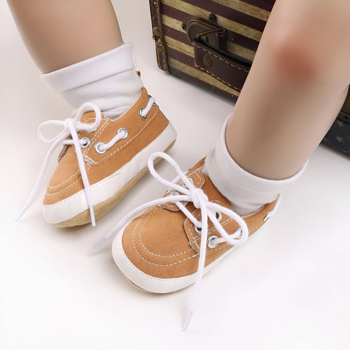 Chaussures bateau marron pour bébé avec lacets blancs, portées avec des chaussettes blanches. Une valise vintage est visible en arrière-plan., 45286825787573,45286825820341,45286825853109,45286825885877,45286825918645,45286825951413,45286825984181,45286826016949,45286826049717,45286826082485,45286826115253,45286826148021
