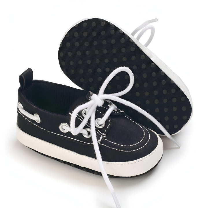 Chaussures bateau pour bébé en noir et blanc avec lacets blancs. Une chaussure est posée à côté de l'autre, montrant le dessous noir avec des cercles pour l'adhérence., 45286825787573,45286825820341,45286825853109,45286825885877,45286825918645,45286825951413,45286825984181,45286826016949,45286826049717,45286826082485,45286826115253,45286826148021