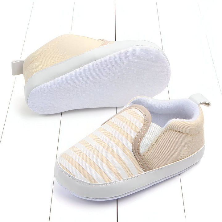 Chaussures de bébé couleur crème à rayures blanches. Une chaussure est retournée, montrant la semelle blanche antidérapante. Chaussures légères et confortables pour les premiers pas de bébé. Mode enfantine, chaussures pour nouveau-né., 45286993297589,45286993330357,45286993363125,45286993395893,45286993428661,45286993461429,45286993494197,45286993526965,45286993559733