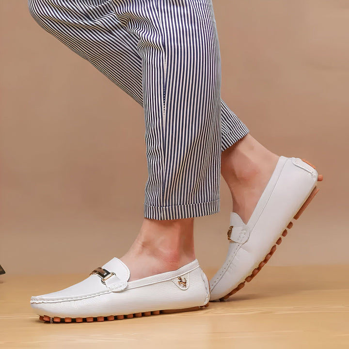 Personne portant des mocassins en cuir blanc avec une boucle dorée, et un pantalon rayé bleu et blanc. Chaussures confortables et élégantes, parfaites pour l'été., 45286790561973,45286790594741,45286790627509,45286790660277,45286790693045,45286790725813,45286790758581