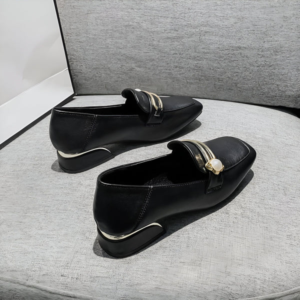 Deux mocassins noirs en cuir sur un coussin gris. Les chaussures sont ornées d'une boucle dorée et d'une perle. Élégance et confort pour toutes les occasions., 45287056277685,45287056310453,45287056343221,45287056375989,45287056408757,45287056441525,45287056474293,45287056507061,45287056539829,45287056572597,45287056605365,45287056638133