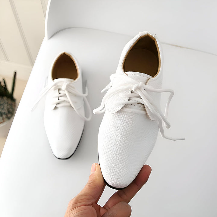 Image de deux chaussures oxford blanches à lacets, style classique, texture peau de serpent, posées sur une chaise blanche. Une main tient une des chaussures., 45287021674677,45287021707445,45287021740213,45287021772981,45287021805749,45287021838517,45287021871285,45287021904053,45287021936821,45287021969589,45287022002357,45287022035125,45287022067893,45287022100661,45287022133429,45287022166197,45287022198965,45287022231733,45287022264501,45287022297269,45287022330037,45287022362805,45287022395573,452