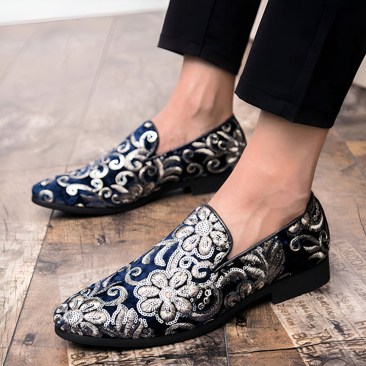 Gros plan sur des mocassins pour hommes en velours bleu marine, ornés de broderies florales dorées et argentées. Un homme porte ces chaussures élégantes sur un plancher en bois., 45286994706613,45286994739381,45286994772149,45286994804917,45286994837685,45286994870453,45286994903221,45286994935989,45286994968757,45286995001525,45286995034293,45286995067061,45286995099829,45286995132597,45286995165365,45286995198133