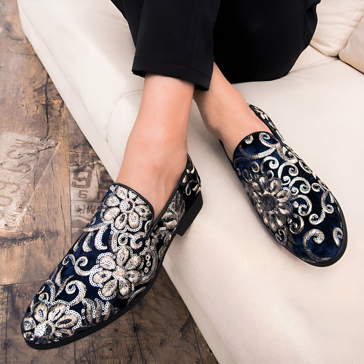 Gros plan sur des mocassins brodés bleu marine et argent avec des motifs floraux, portés par une personne assise sur un canapé blanc. Chaussures élégantes et luxueuses., 45286994706613,45286994739381,45286994772149,45286994804917,45286994837685,45286994870453,45286994903221,45286994935989,45286994968757,45286995001525,45286995034293,45286995067061,45286995099829,45286995132597,45286995165365,45286995198133