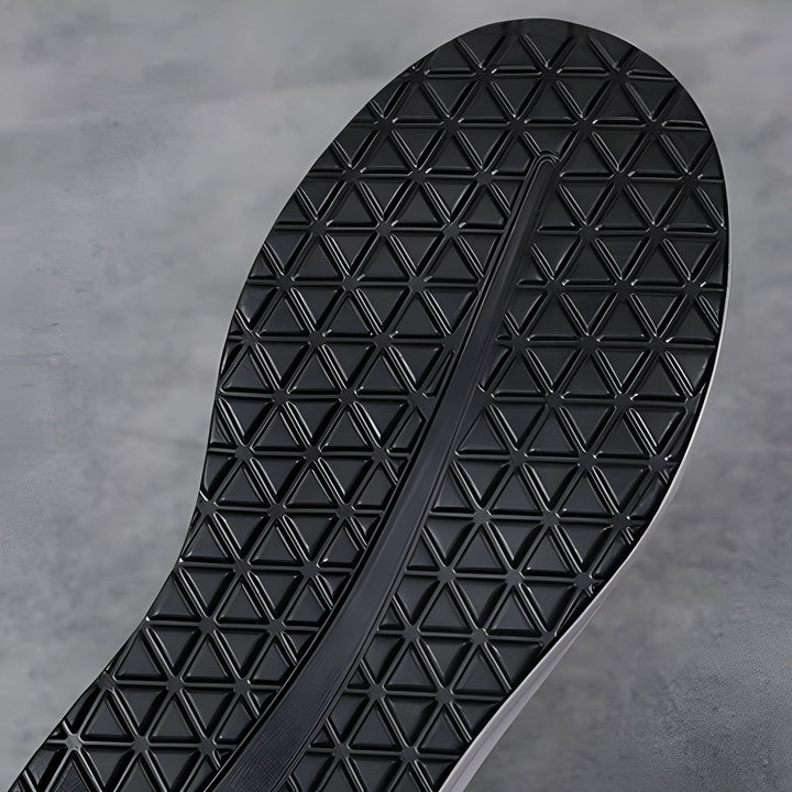 Gros plan de la semelle d'une chaussure. La semelle est en caoutchouc noir avec un motif de triangles en relief pour l'adhérence. Une rainure longitudinale traverse le centre., 45286645989557,45286646022325,45286646055093,45286646087861,45286646120629,45286646153397,45286646186165,45286646218933,45286646251701,45286646284469,45286646317237,45286646350005,45286646382773,45286646415541