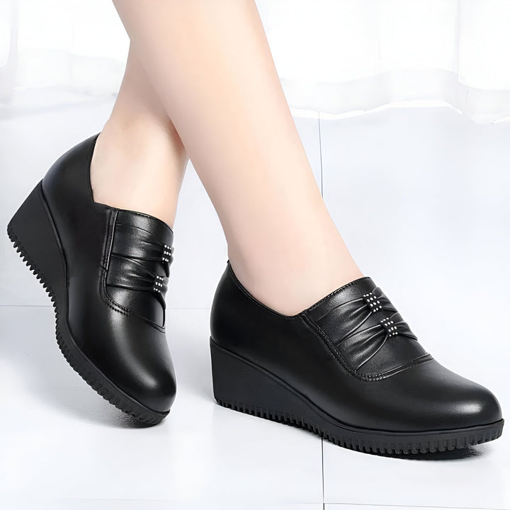 Gros plan sur des pieds portant des chaussures compensées noires élégantes. Chaussures en cuir noir avec détail plissé et décoratif. Idéales pour un look professionnel et confortable., 45286793347253,45286793380021,45286793412789,45286793445557,45286793478325,45286793511093,45286793543861