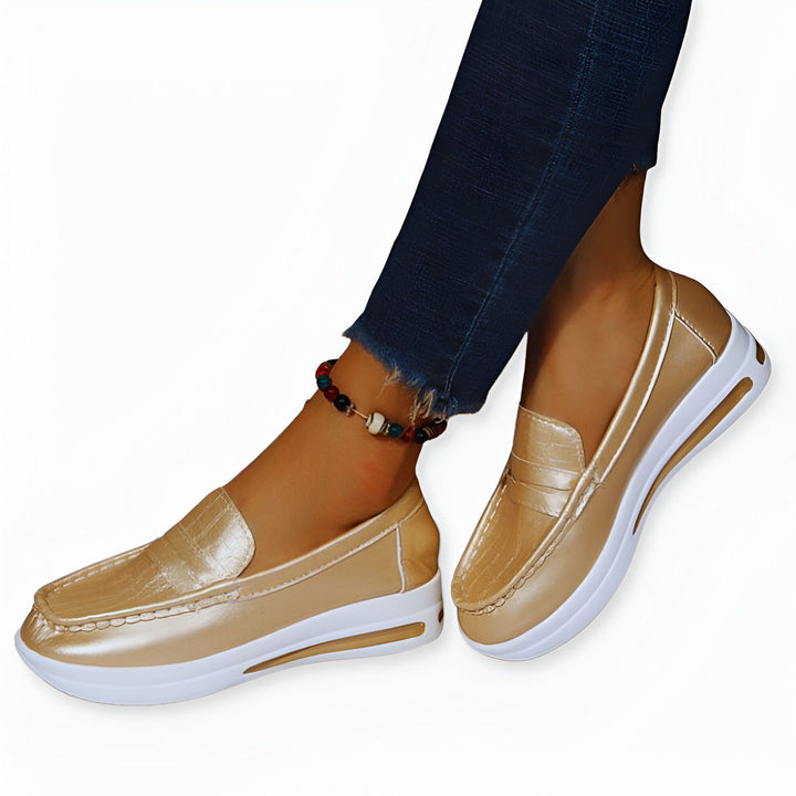 Gros plan sur des mocassins couleur or à semelle blanche portés avec un jean et une chaîne de cheville. Chaussures confortables pour femmes., 45286870778037,45286870810805,45286870843573,45286870876341,45286870909109,45286870941877,45286870974645,45286871007413,45286871040181,45286871072949,45286871105717,45286871138485,45286871171253,45286871204021,45286871236789,45286871269557,45286871302325,45286871335093,45286871367861,45286871400629,45286871433397,45286871466165,45286871498933,45286871531701,45286