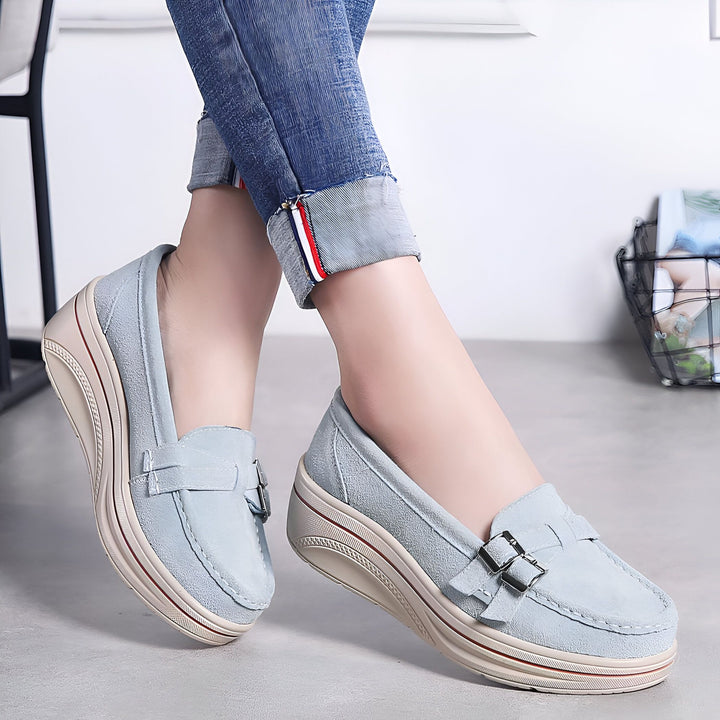 Gros plan de chaussures compensées bleu clair en daim aux pieds d'une femme portant un jean retroussé. Les chaussures ont une boucle décorative et une semelle beige à rayures rouges., 45286912786613,45286912819381,45286912852149,45286912884917,45286912917685,45286912950453,45286912983221,45286913015989,45286913048757,45286913081525,45286913114293,45286913147061,45286913179829,45286913212597,45286913245365,45286913278133,45286913310901,45286913343669,45286913376437,45286913409205,45286913441973,4528691