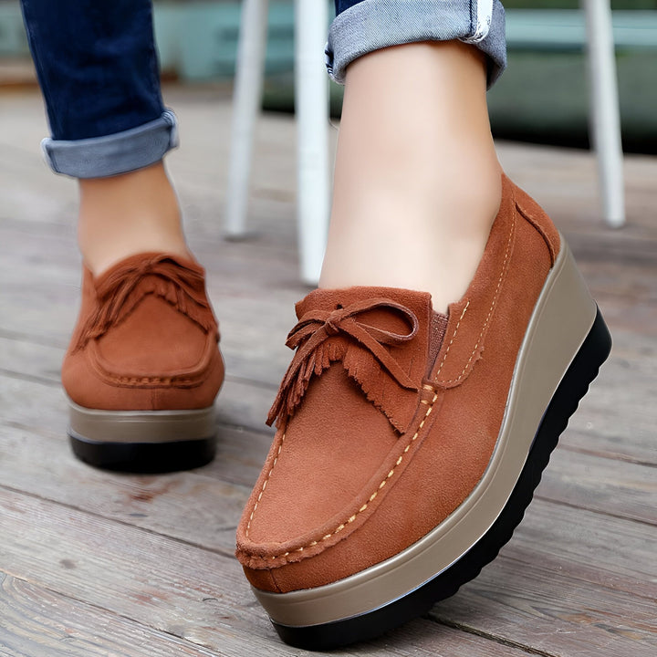Gros plan de chaussures compensées marron en daim avec nœud à franges sur pieds féminins, portées avec un jean bleu. Sol en bois visible., 45286964887733,45286964920501,45286964953269,45286964986037,45286965018805,45286965051573,45286965084341,45286965117109,45286965149877,45286965182645,45286965215413,45286965248181,45286965280949,45286965313717,45286965346485,45286965379253,45286965412021,45286965444789,45286965477557,45286965510325,45286965543093,45286965575861,45286965608629,45286965641397