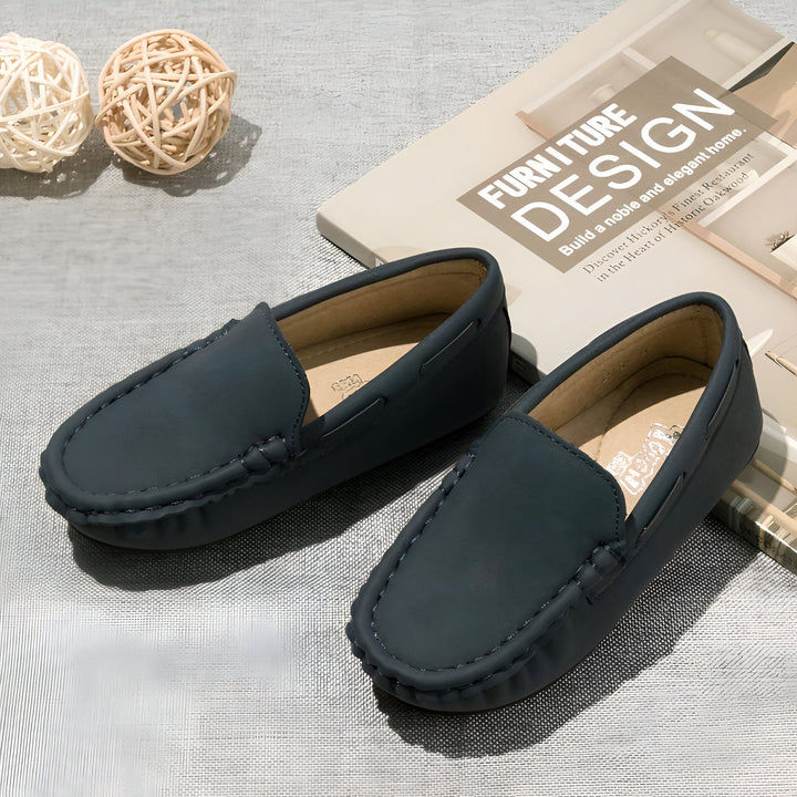 Mocassins bleus en cuir pour enfants, posés à côté d'un livre de design d'intérieur et de boules décoratives en osier sur une surface grise texturée. Chaussures élégantes pour garçons., 45287100252341,45287100285109,45287100317877,45287100350645,45287100383413,45287100416181,45287100448949,45287100481717,45287100514485,45287100547253,45287100580021,45287100612789,45287100645557,45287100678325,45287100711093,45287100743861,45287100776629,45287100809397,45287100842165,45287100874933,45287100907701