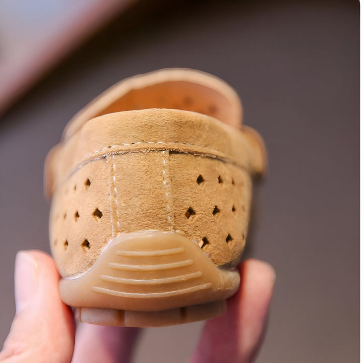 Vue rapprochée d'une chaussure enfant en cuir beige avec des perforations en forme de losange. La semelle est en caoutchouc marron et la chaussure est maintenue par une main., 45286761824437,45286761857205,45286761889973,45286761922741,45286761955509,45286761988277,45286762021045,45286762053813,45286762086581,45286762119349,45286762152117,45286762184885,45286762217653,45286762250421,45286762283189,45286762315957,45286762348725,45286762381493,45286762414261,45286762447029,45286762479797,45286762512565,452