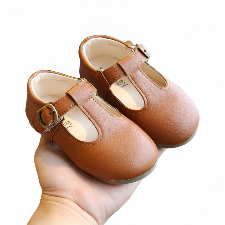 Une main tenant une paire d'élégantes chaussures pour bébés de couleur marron avec des brides et des boucles dorées., 45287038910645,45287038943413,45287038976181,45287039008949,45287039041717,45287039074485,45287039107253,45287039140021,45287039172789,45287039205557,45287039238325,45287039271093,45287039303861,45287039336629,45287039369397,45287039402165,45287039434933,45287039467701,45287039500469,45287039533237,45287039566005,45287039598773,45287039631541,45287039664309,45287039697077,452870397298