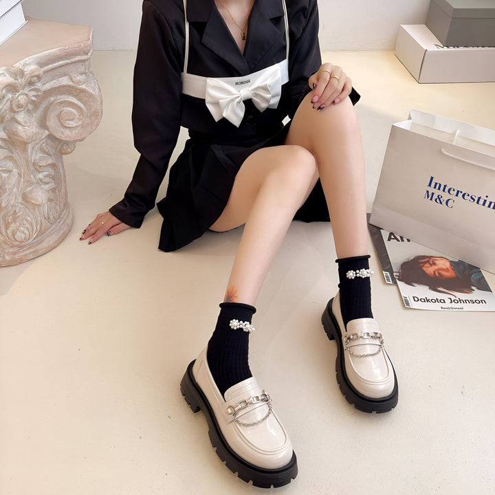 Femme assise, portant une veste noire avec un nœud blanc, des chaussettes noires avec des perles et des mocassins en cuir blanc avec des chaînes. Sac de magasinage et magazine à proximité., 45286868418741,45286868451509,45286868484277,45286868517045,45286868549813,45286868582581,45286868615349,45286868648117,45286868680885,45286868713653,45286868746421,45286868779189