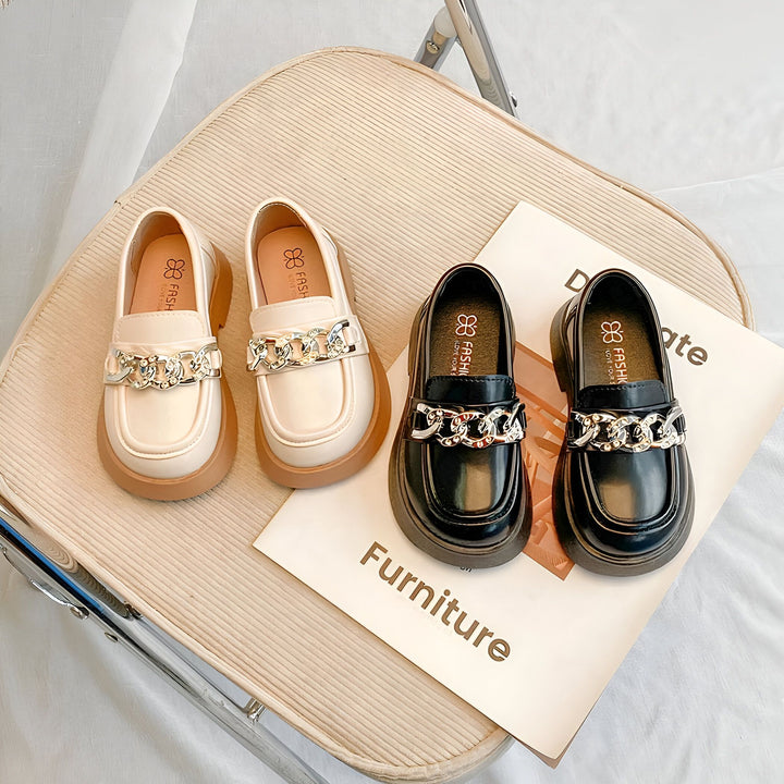 Deux paires de mocassins pour enfants, une beige et une noire, ornées de chaînes argentées, reposent sur une chaise en velours côtelé avec un magazine de meubles. Chaussures élégantes pour enfants, mode enfantine, mocassins avec chaîne., 45287036944565,45287036977333,45287037010101,45287037042869,45287037075637,45287037108405,45287037141173,45287037173941,45287037206709,45287037239477,45287037272245,45287037305013,45287037337781,45287037370549,45287037403317,45287037436085,45287037468853,452870375