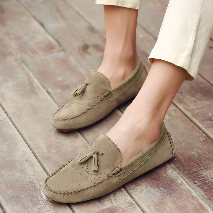 Homme portant des mocassins en daim marron clair avec des glands, assis sur un plancher en bois. Chaussures décontractées, mode masculine., 45286802882741,45286802915509,45286802948277,45286802981045,45286803013813,45286803046581,45286803079349