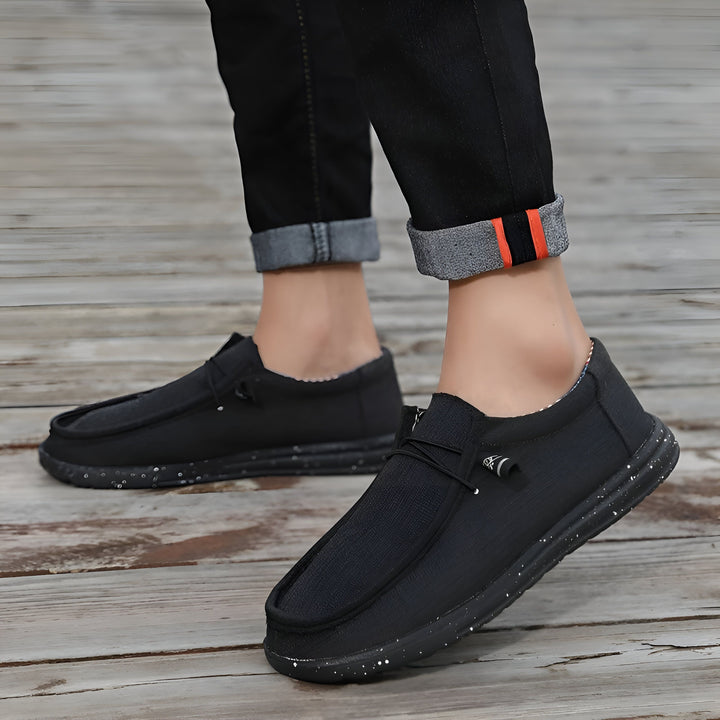 Gros plan de chaussures décontractées noires portées avec un jean retroussé. Chaussures type mocassins en toile noire, semelles mouchetées de blanc, lacets décoratifs. Idéales pour un style décontracté et confortable., 45286675710133,45286675742901,45286675775669,45286675808437,45286675841205,45286675873973,45286675906741,45286675939509,45286675972277,45286676005045,45286676037813,45286676070581,45286676103349,45286676136117,45286676168885,45286676201653,45286676234421,45286676267189,452866762999