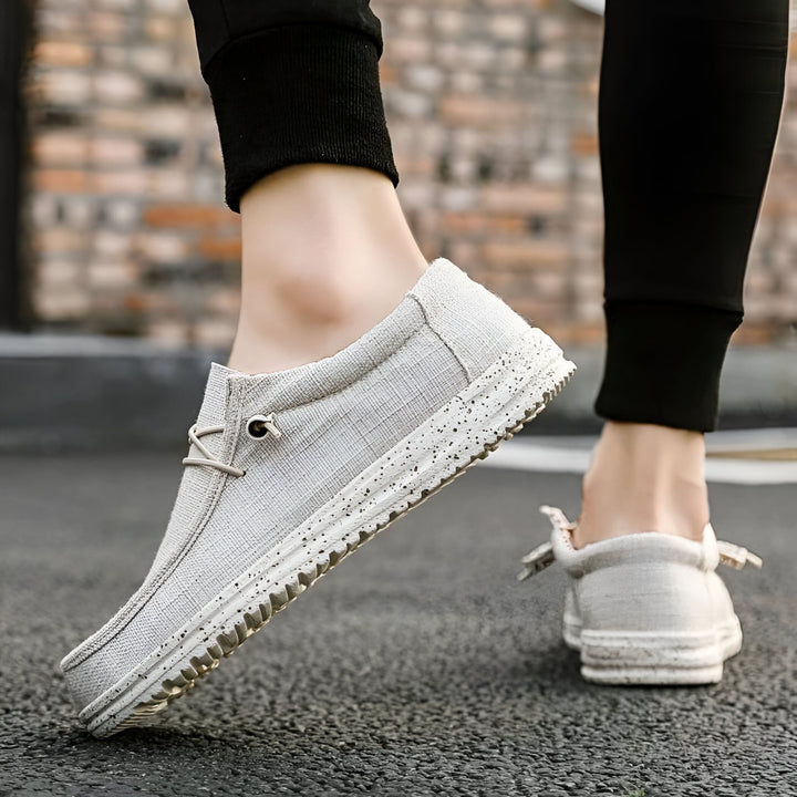 Gros plan d'une personne portant des chaussures décontractées grises en toile, sans lacets visibles, avec une semelle épaisse et texturée. Style moderne et confortable., 45286731415733,45286731448501,45286731481269,45286731514037,45286731546805,45286731579573,45286731612341,45286731645109,45286731677877,45286731710645,45286731743413,45286731776181,45286731808949,45286731841717,45286731874485,45286731907253,45286731940021,45286731972789,45286732005557,45286732038325,45286732071093,45286732103861