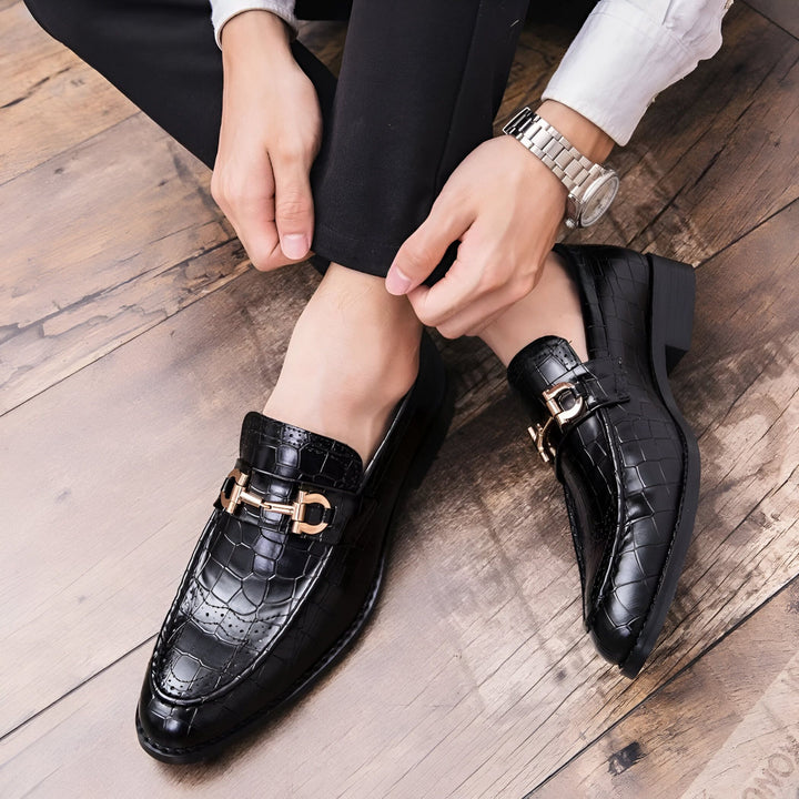 Gros plan sur une personne portant des mocassins en cuir noir avec des boucles dorées. Le pantalon noir et la montre-bracelet complètent le look élégant. Le fond est un parquet en bois., 45286694322357,45286694355125,45286694387893,45286694420661,45286694453429,45286694486197,45286694518965,45286694551733,45286694584501,45286694617269,45286694650037,45286694682805,45286694715573,45286694748341,45286694781109,45286694813877,45286694846645,45286694879413,45286694912181,45286694944949