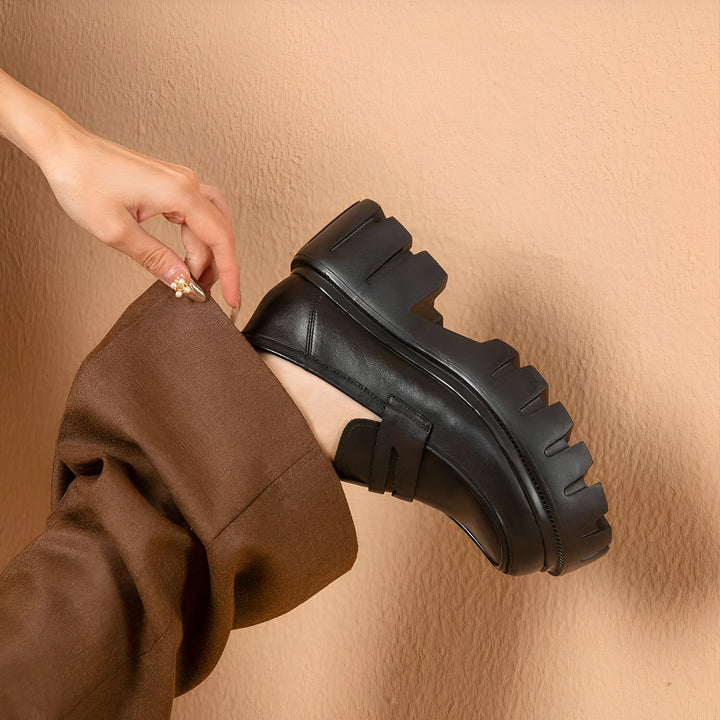 Gros plan d'une personne ajustant une chaussure noire à plateforme. Le mocassin en cuir épais contraste avec le pantalon marron ample et le fond beige texturé. Détail soigné de la manucure avec un ornement floral., 45287144325301,45287144358069,45287144390837,45287144423605,45287144456373,45287144489141,45287144521909,45287144554677,45287144587445,45287144620213,45287144652981,45287144685749