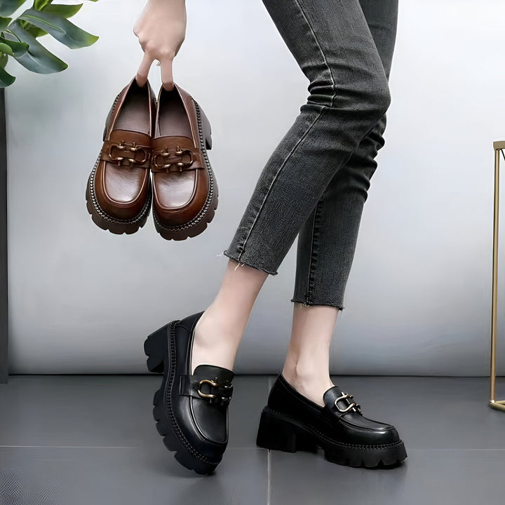 Une femme porte des mocassins noirs à semelles épaisses et tient une paire de mocassins marron identiques. Les chaussures ont une boucle décorative., 45286850461877,45286850494645,45286850527413,45286850560181,45286850592949,45286850625717,45286850658485,45286850691253,45286850724021,45286850756789,45286850789557,45286850822325