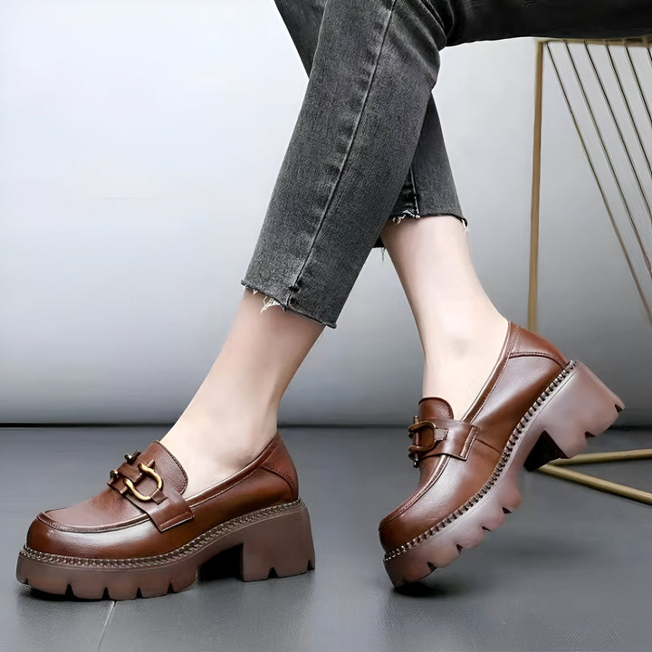 Une femme porte des mocassins marron à plateforme avec une boucle dorée. Elle porte un jean gris foncé. Chaussures élégantes, mode automne/hiver., 45286850461877,45286850494645,45286850527413,45286850560181,45286850592949,45286850625717,45286850658485,45286850691253,45286850724021,45286850756789,45286850789557,45286850822325