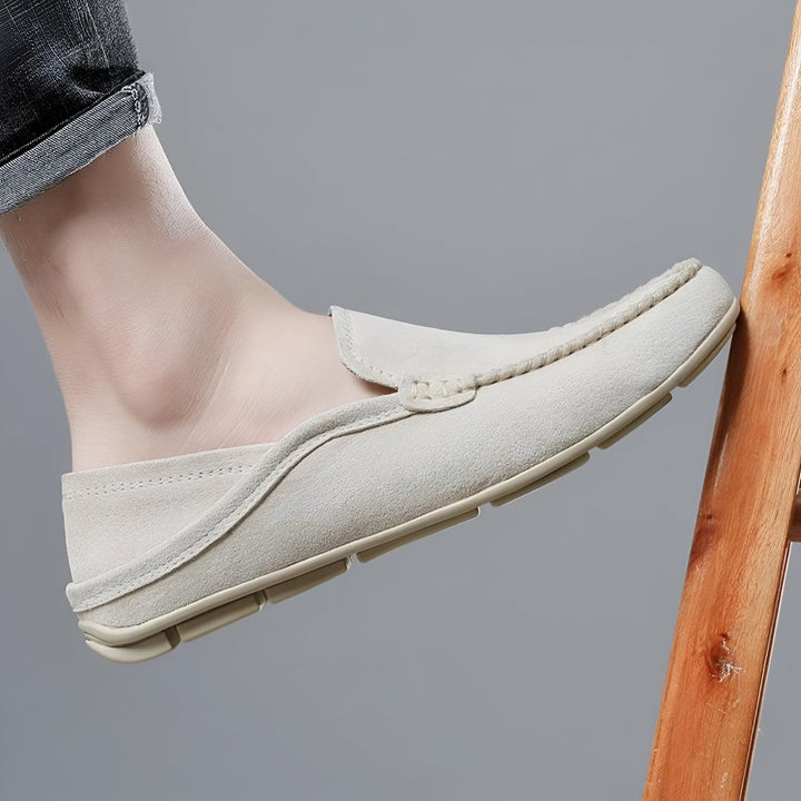 Gros plan d'un mocassin beige en daim porté par un homme, appuyé contre une chaise en bois. Chaussure décontractée et élégante, idéale pour le printemps et l'été. Mode masculine., 45286729711797,45286729744565,45286729777333,45286729810101,45286729842869,45286729875637,45286729908405,45286729941173,45286729973941,45286730006709,45286730039477,45286730072245,45286730105013,45286730137781,45286730170549,45286730203317,45286730236085,45286730268853,45286730301621,45286730334389