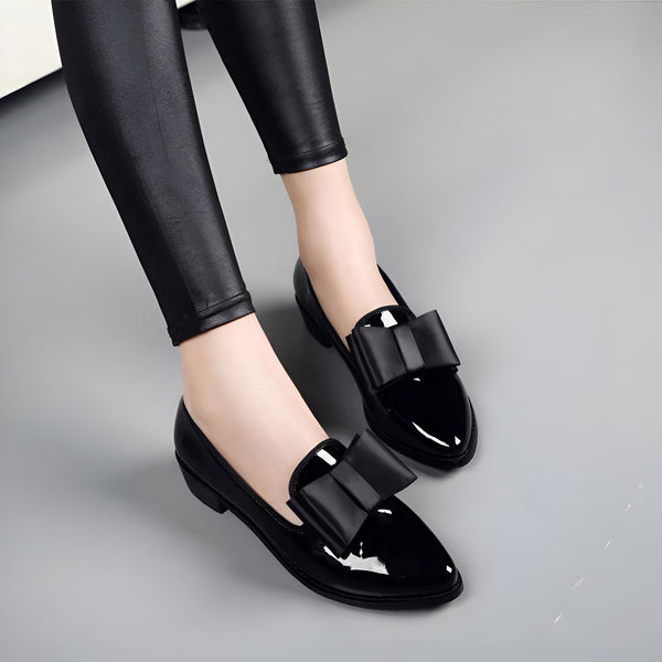 Gros plan de pieds portant des chaussures plates noires vernies à nœud papillon, associées à un legging en cuir noir brillant. Style élégant et tendance., 45286907478197,45286907510965,45286907543733,45286907576501,45286907609269,45286907642037,45286907674805,45286907707573,45286907740341,45286907773109,45286907805877,45286907838645,45286907871413,45286907904181