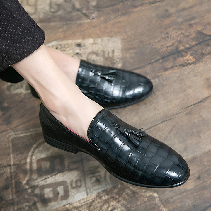 Gros plan sur des mocassins noirs en cuir façon croco avec glands, portés sur un parquet en bois. Chaussures élégantes pour hommes., 45287059095733,45287059128501,45287059161269,45287059194037,45287059226805,45287059259573,45287059292341,45287059325109,45287059357877,45287059390645