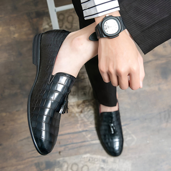Gros plan sur des mocassins noirs à glands avec motif peau de crocodile portés par un homme en costume. La montre à son poignet ajoute une touche d'élégance. Chaussures de ville pour homme, style et sophistication., 45287059095733,45287059128501,45287059161269,45287059194037,45287059226805,45287059259573,45287059292341,45287059325109,45287059357877,45287059390645