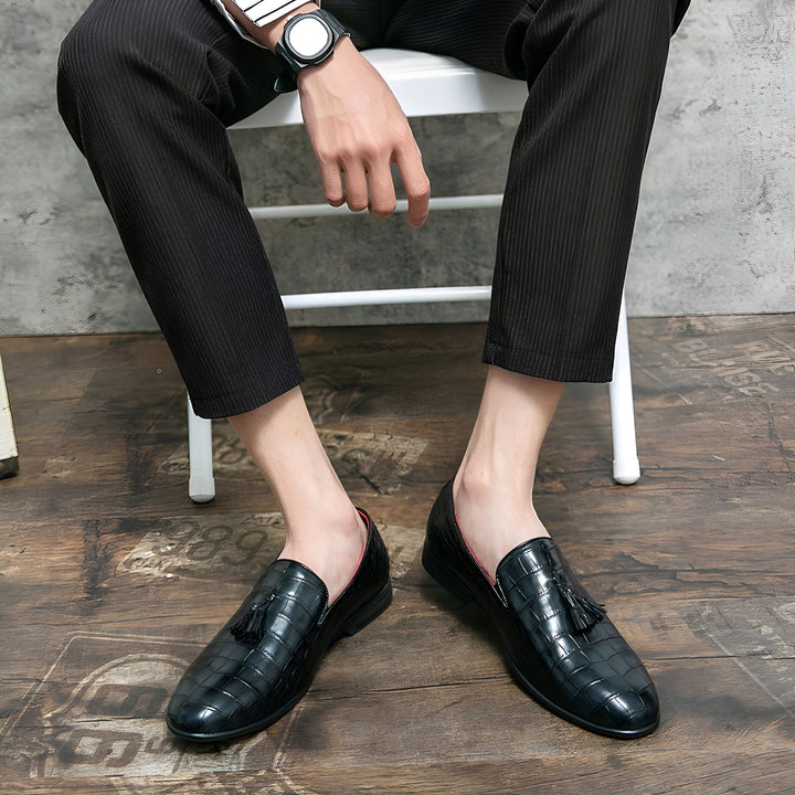 Homme assis sur une chaise, portant un pantalon rayé et des mocassins en cuir noir texturé avec des glands. Montre-bracelet visible. Style élégant et décontracté. Chaussures de ville pour homme., 45287059095733,45287059128501,45287059161269,45287059194037,45287059226805,45287059259573,45287059292341,45287059325109,45287059357877,45287059390645